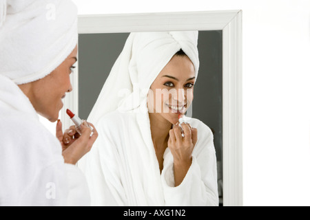 Schöne junge Frau anziehen Lippenstift vor dem Spiegel mit einem Handtuch auf ihr Haar Stockfoto