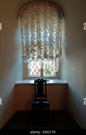 Sonnenlicht Licht durch ein Fenster bedeckt mit alten altmodischen net Stil Vorhänge mit einem Stuhl vor Stockfoto
