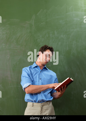 Lehrer mit Buch vor der Tafel Stockfoto