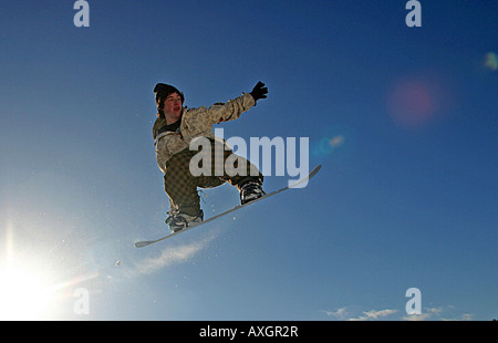 Ein farbiges horizontales Bild, das ein durch die Luft rasendes Snowboard zeigt, bei dem Schnee von der Schneebrette und Sonnenbrände auf dem Bild zu sehen sind. Stockfoto