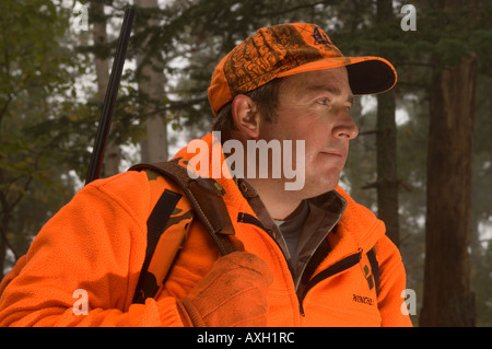 PORTRÄT VON DEER HUNTER BLAZE ORANGE MIT GEWEHR AUF DEM RÜCKEN IM NÖRDLICHEN MINNESOTA NEBLIGEN WALD Stockfoto