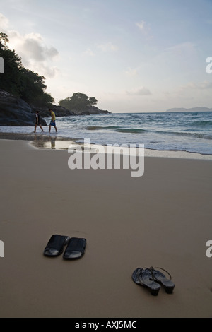 Sandalen auf den Strand von Tioman Island in der Nähe von Teluk Salang Dorf, während die Besitzer in der Ferne links paddeln. Tioman Island. Stockfoto