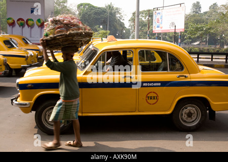 Ein gelbes Taxi fährt in Kolkata Chowringee Bezirk im Herzen der Stadt. Eine Hawker geht es vorbei an den Verkehr mit einem Korb. Stockfoto