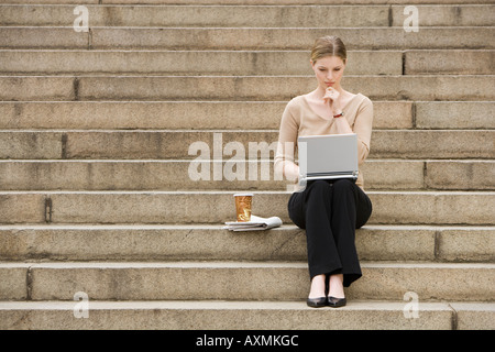 Junge Frau sitzt im Freien auf Treppen mit laptop Stockfoto