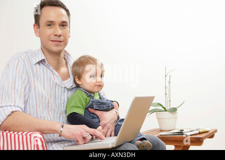 Vater mit Sohn und Laptop bei Lap Blick in die Kamera Stockfoto
