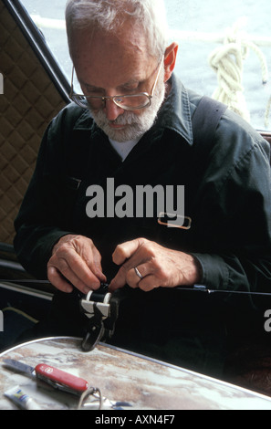 Ein älterer, älterer Alaskan-Fliegenfischer mit weißem Bart bindet eine Fliege an eine Angelrutenschnur seines Lachsfischerkabels. Stockfoto