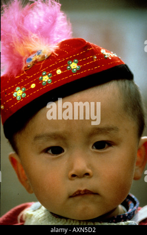 ansprechende Mandarin Baby in Dunhuang, einer der westlichen China Minderheit Menschen tragen traditionelle Federhut Stockfoto