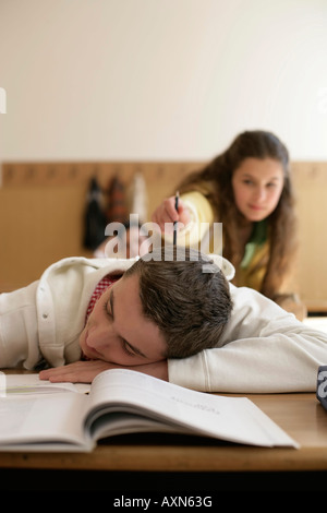 Teenager-Jungen schlafen in einem Klassenzimmer, Teenager-Mädchen auf ihn tippen Stockfoto