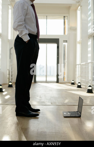 Laptop auf einem Boden neben den Beinen eines Kaufmanns Stockfoto