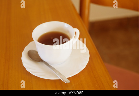 Halb volle Tasse Kaffee oder Tee mit Untertasse und Teelöffel auf einen Tisch mit einem leeren Stuhl Stockfoto