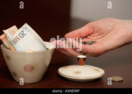 Hand mit Münzen vor eine Zuckerdose gefüllt mit Euro-Scheine (Teil), Nahaufnahme Stockfoto