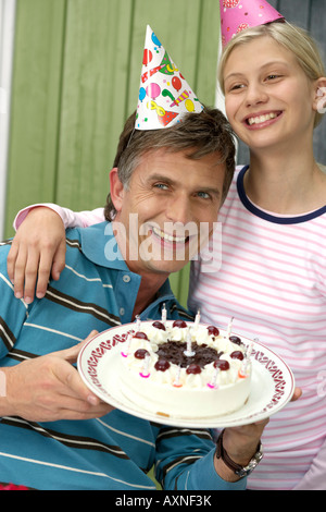 Reifen Mann mit einer Geburtstagstorte in der Hand neben seiner blonden Tochter, beide tragen Hörner, close-up Stockfoto