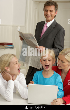 Vater mit finanziellen Papier Blick auf seine beiden Töchter, die neben ihrer Mutter hinter einem Laptop sitzen Stockfoto