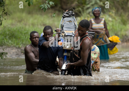 Eine Gruppe von Männern tragen ein Motorrad über einen überquellenden Fluss Stockfoto