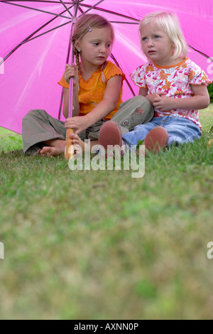 Zwei kleine Mädchen sitzen unter einer rosa Regenschirm Stockfoto