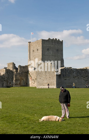 Ein Mann spielt mit einem Hund auf dem Gelände des Portchester Castle mit der Bergfried im Hintergrund Stockfoto