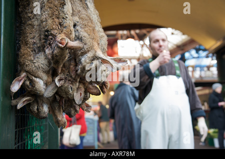 Hasen zum Verkauf in London Borough Market, während ein Fischhändler aufgereiht zündet sich eine Zigarette in den Hintergrund. Stockfoto