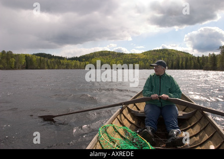 Eine ältere finnische Frau rudert ein hölzernes Ruderboot / Skiff / Schlauchboot an einem See in Finnland Stockfoto