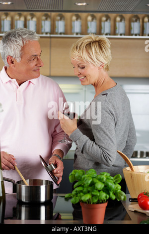 Blonde Frau mit einem Glas Wein in der Hand wacht einen Mann kocht Stockfoto