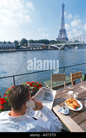 Mann am Ufer Hausboot mit dem Frühstück am Tisch am Telefon sprechen und lesen die Zeitung am Morgen in Paris Stockfoto