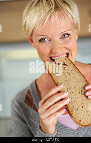 Reife Frau mit blonden Haaren Biss in ein Stück Brot, Nahaufnahme Stockfoto