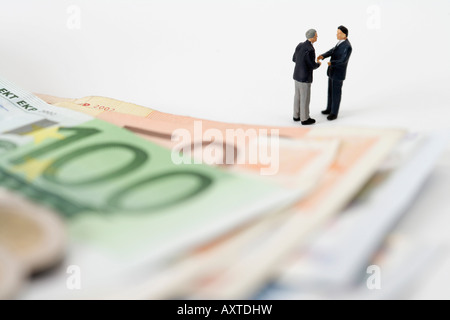 Zwei Geschäftsleute Figuren Händeschütteln, Euro-Banknoten im Vordergrund Stockfoto