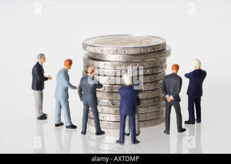 Gruppe von Geschäftsleuten Figuren um einen Stapel von Münzen Stockfoto