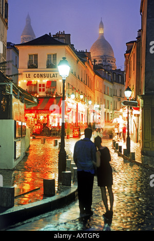 Paar, umarmen, auf nasser Straße mit Kopfsteinpflaster in der Nacht in Montmartre mit Sacre Coeur über Hochhäuser in Paris Stockfoto