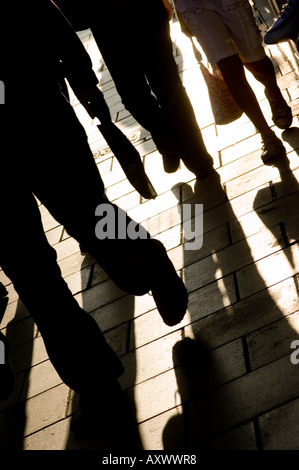 Silhouetten und Schatten von Käufern zu Fuß auf dem Bürgersteig auf der Straße in einer Stadt oder Gemeinde Stockfoto