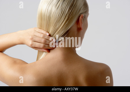 Magere junge Frau hält ihr blondes Haar, Rückansicht Stockfoto