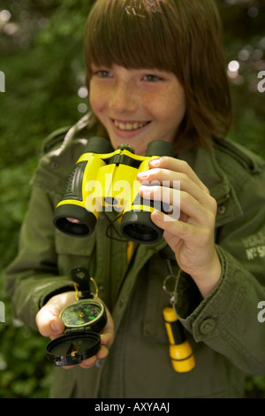 ein Junge lächelt, als er spielt im Wald mit seinem Fernglas und Kompass Stockfoto