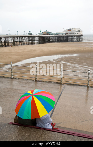 Paar Zuflucht vor dem Regen auf Blackpool Promenade mit Blick zum Nordpier Stockfoto