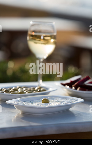 Hohes Glas Weißwein, Tzatziki Salat mit grünen Oliven, Teller mit grünen Oliven, rote Beete Salat auf Marmortisch Meer Stockfoto