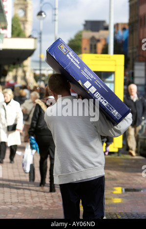 Mann trägt schwere Kiste auf seiner Schulter in Fußgängerzone im Stadtzentrum von Belfast Stockfoto