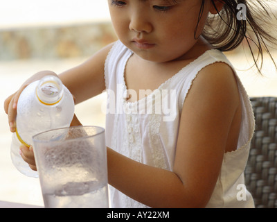 Nahaufnahme eines Mädchens gießt Wasser aus einer Flasche Wasser in einem Glas Stockfoto