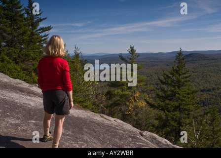 Eine Frau in einem roten t-Shirt steht auf einem Felsvorsprung auf der Eule Kopf Berg Blick auf See und Berge in der Ferne. Stockfoto