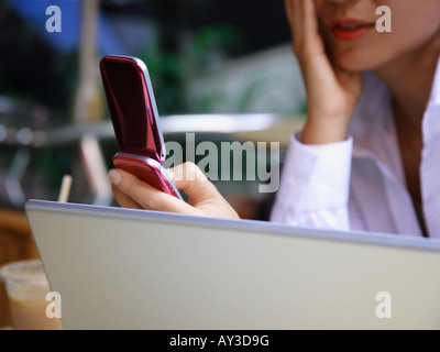 Eine Geschäftsfrau vor einem Laptop sitzen und mit Hilfe eines Mobiltelefons in Nahaufnahme Stockfoto