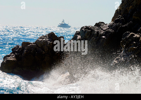 Wellen auf den Felsen von Shore, Schiff im Hintergrund. Stockfoto
