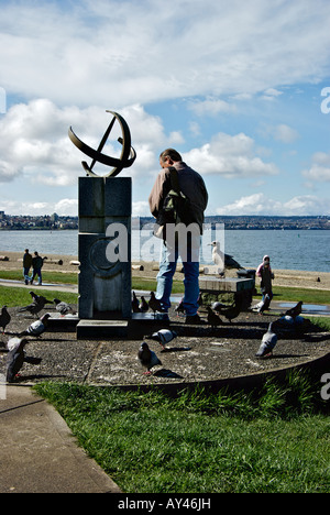 Mann, die Vögel zu füttern, bei Sonnenuhr Bildhauerei an der English Bay Strand im West End von Vancouver British Columbia Kanada Stockfoto