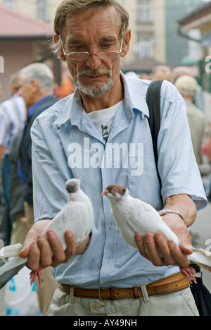 Mann mit Brille hält zwei weiße, racing Tauben oder Tauben in einem Straßenmarkt in Polen Stockfoto