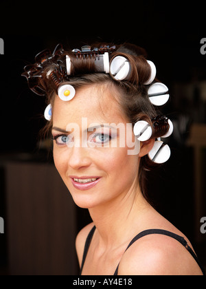 Porträt von einem schönen Brünette Mädchen mit Rollen im Haar vor einem dunklen Hintergrund Stockfoto