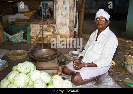 Ein Lebensmittelhändler hocken neben Skalen in einem Straßenmarkt, Madurai, Tamil Nadu, Indien Stockfoto