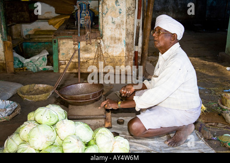 Ein Lebensmittelhändler hocken neben Skalen in einem Straßenmarkt, Madurai, Tamil Nadu, Indien Stockfoto