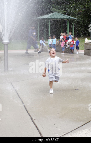 4 Jahre alter Junge läuft durch eine Wasser-Sprinkleranlage auf einem Spielplatz Stockfoto