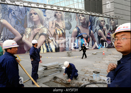 Arbeitnehmer ebnen Fliesen vor einer riesigen PRADA Plakatwand am Shin Kong Place in Beijing CBD. 3. April 2008 Stockfoto