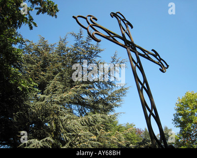 Gusseisen Kreuz am Kirchhof gegen Baum Blätter Stockfoto