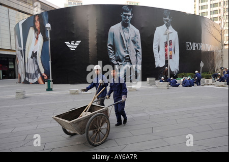 Chinesische Arbeiter ebnen Fliesen vor eine riesige Plakatwand von Emporio Armani in Beijing CBD, China. 3. April 2008 Stockfoto