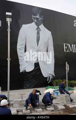 Chinesische Arbeiter ebnen Fliesen vor eine riesige Plakatwand von Emporio Armani in Beijing CBD, China. 3. April 2008 Stockfoto