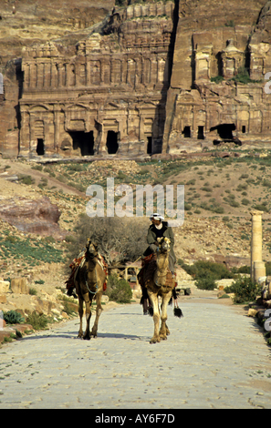 Mann reitet ein Kamel auf einer gepflasterten Straße nahe dem Eingang auf die königlichen Gräber geschnitzt in den Klippen von Petra, Jordanien. Stockfoto