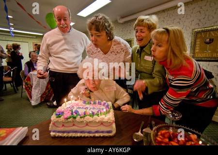 Unterstützt von Familie und Freunden, die einen hundertjährigen, die Kerzen auf ihrem Kuchen während ihrem 100. Geburtstag in einem Pflegeheim bläst Stockfoto